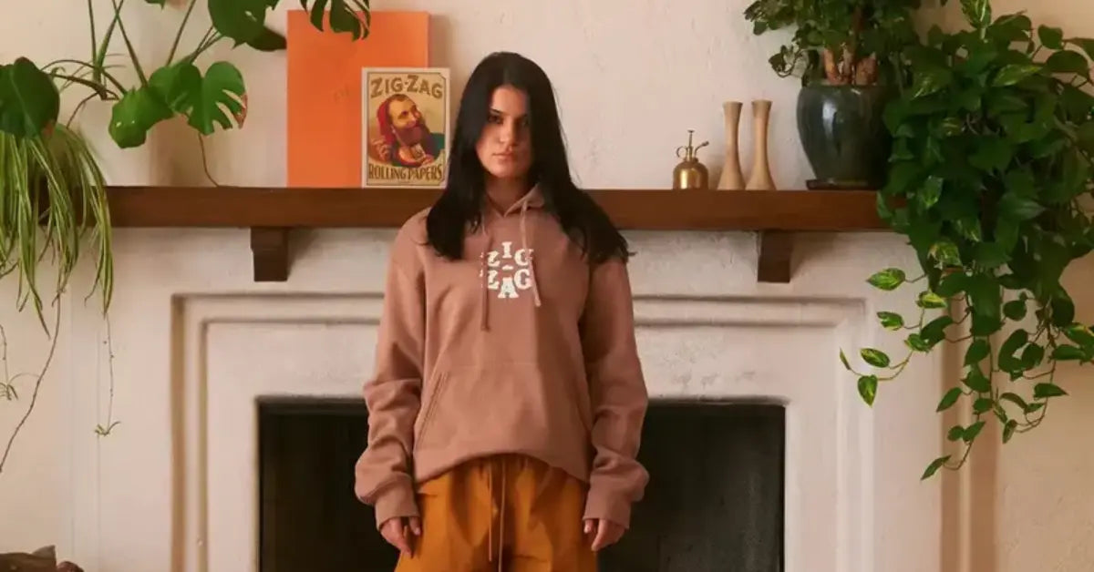 Woman wearing a brown Zig-Zag Vertex Hoodie stands in front of a shelf with plants and Zig-Zag decor
