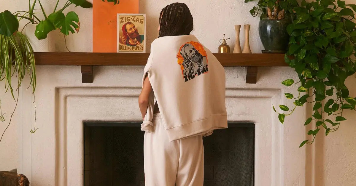 Back view of a woman wearing a cream Zig-Zag sweatshirt draped over her shoulders, standing by a fireplace