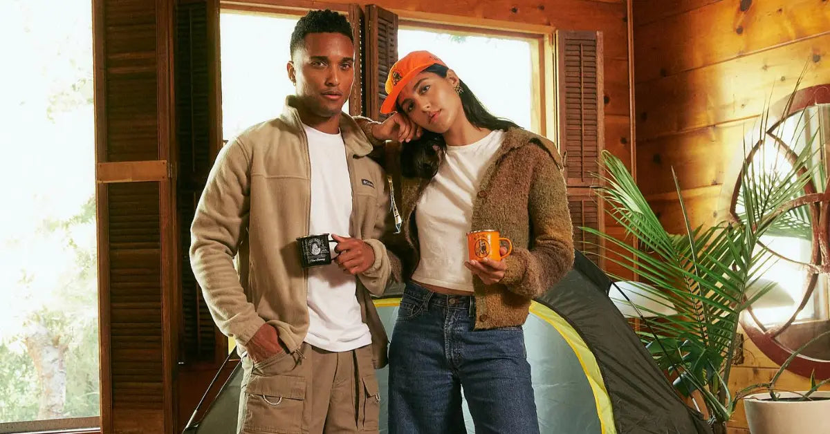 Vintage clothing look with a cozy cabin vibe, featuring layered outerwear, denim, and retro-style mugs by a tent indoors