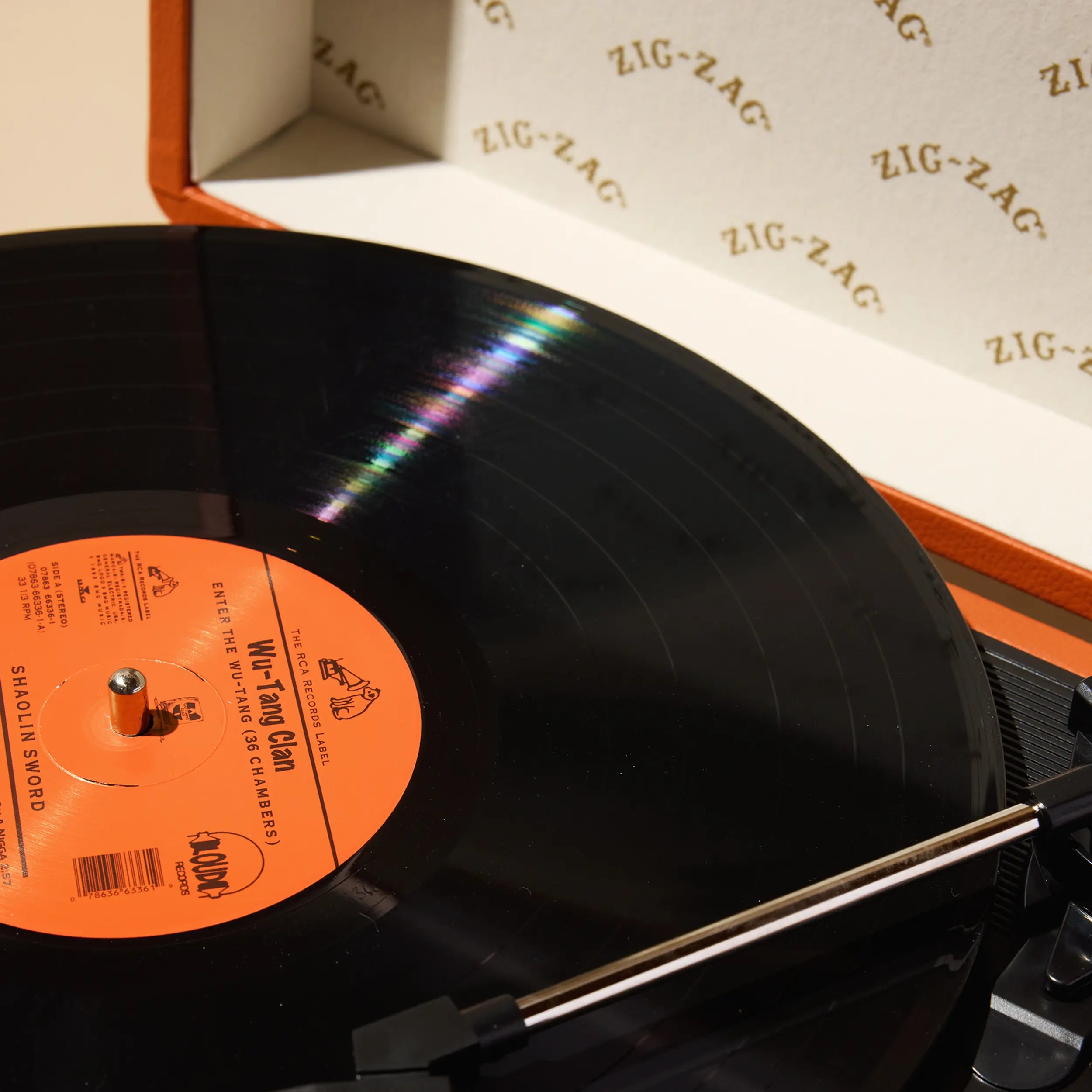 Close-up of a Zig Zag record player spinning a Wu-Tang Clan vinyl with branded inner lid and orange turntable case.