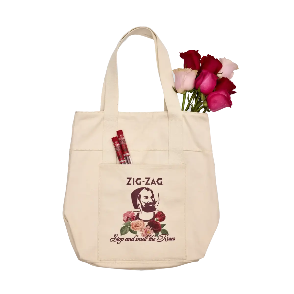 Zig-Zag cream tote bag featuring a vintage logo, rose graphic, and "Stop and smell the Roses" text, holding flowers and accessories.