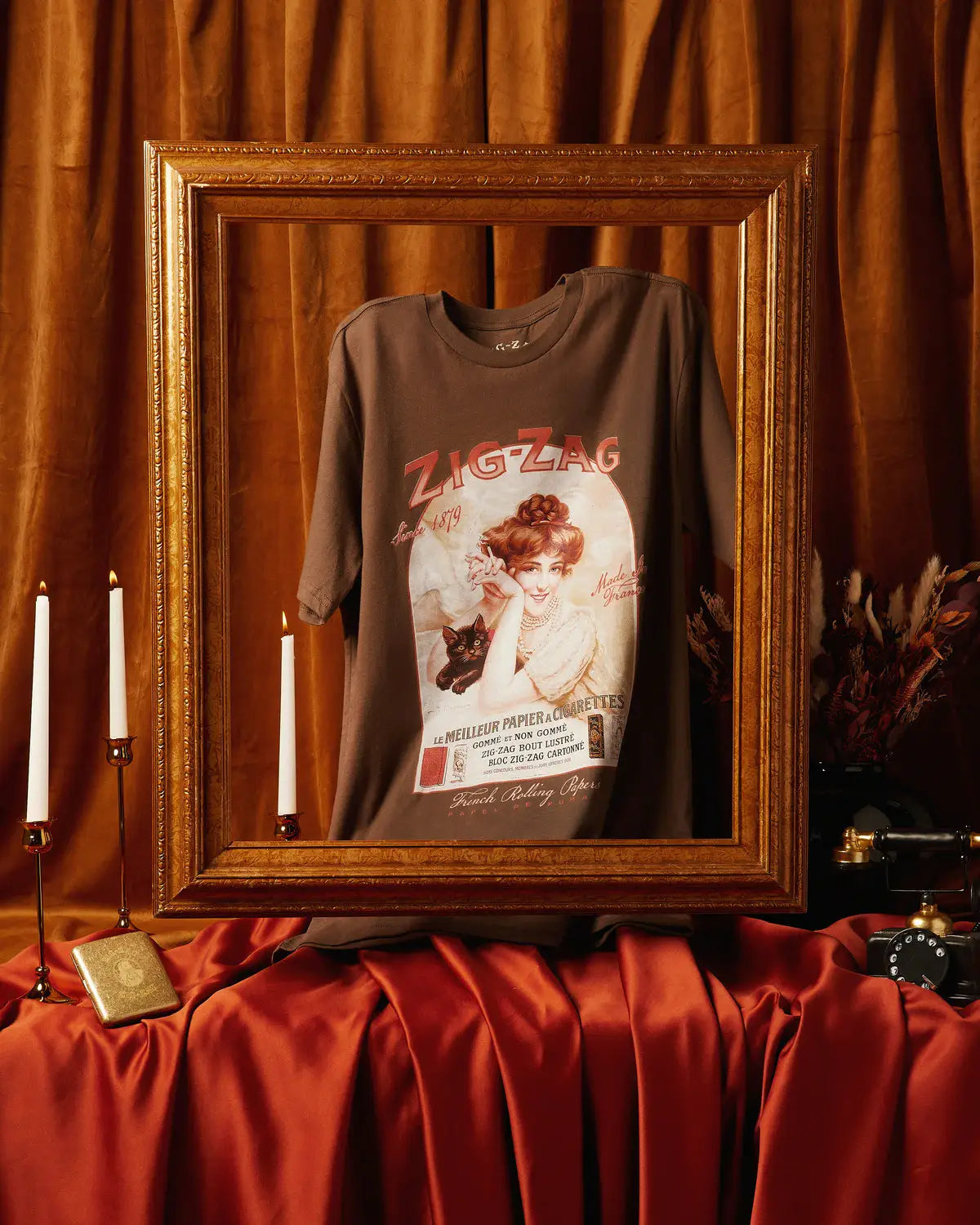 Zig-Zag vintage-style graphic T-shirt displayed in an ornate frame with elegant candlelit decor and rich fabric.