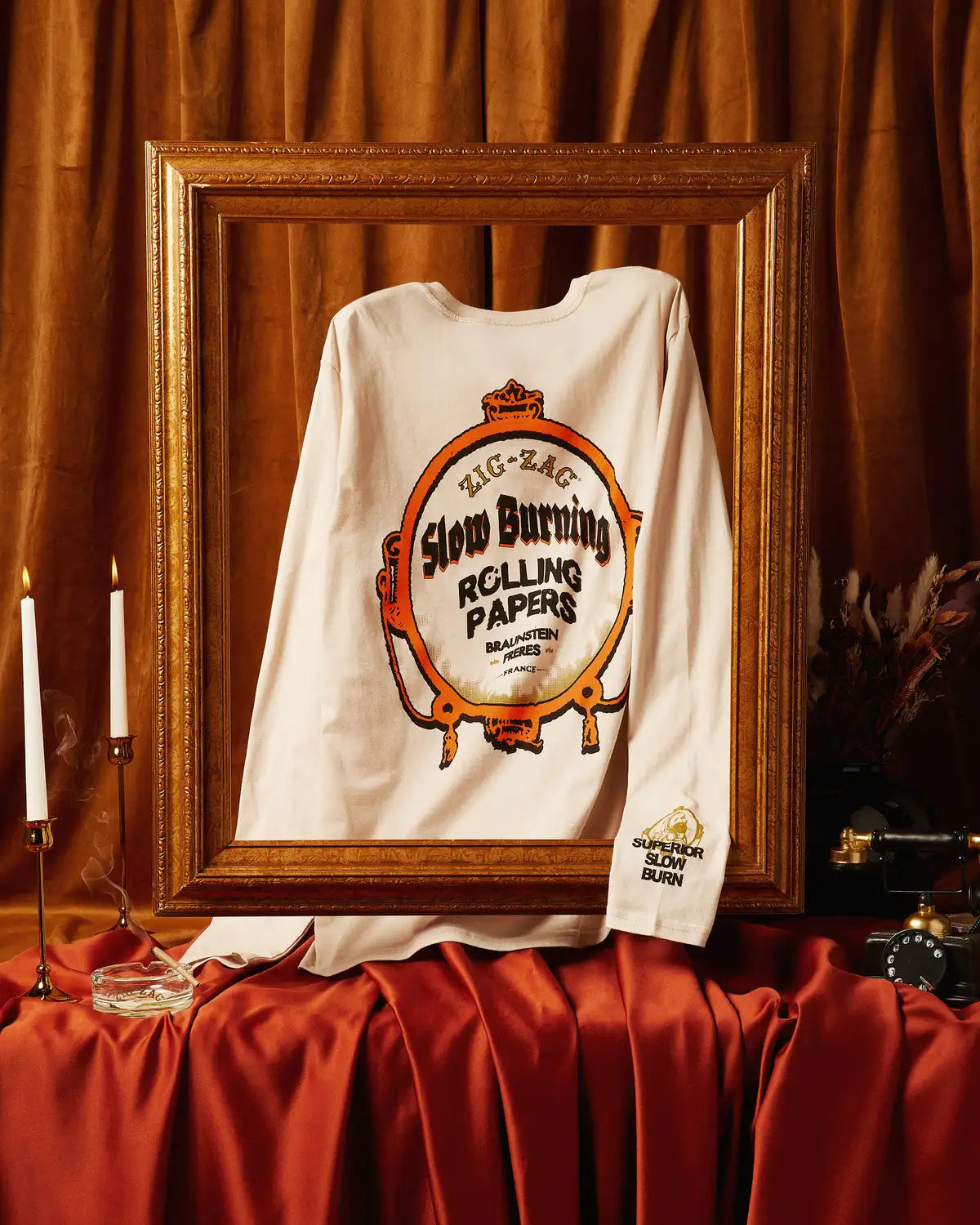 Zig-Zag long-sleeve white shirt featuring a bold vintage "Slow Burning Rolling Papers" graphic displayed in an ornate frame with elegant decor.