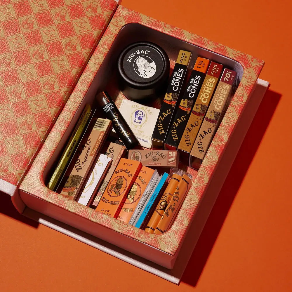 Zig-Zag stash book filled with rolling papers, cones, and accessories displayed on an orange surface.
