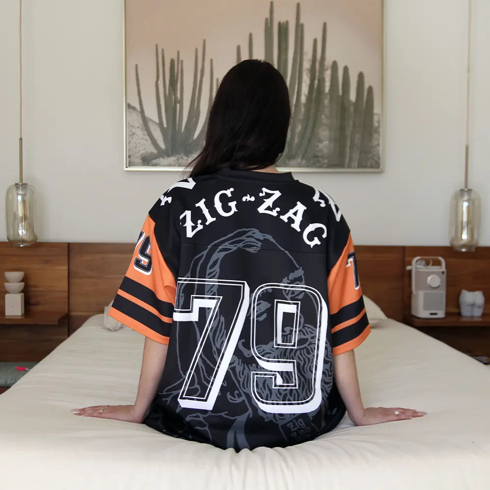 Zig Zag black jersey with large number 79 and bold back print featuring vintage branding and orange-striped sleeves, worn casually on a bed.