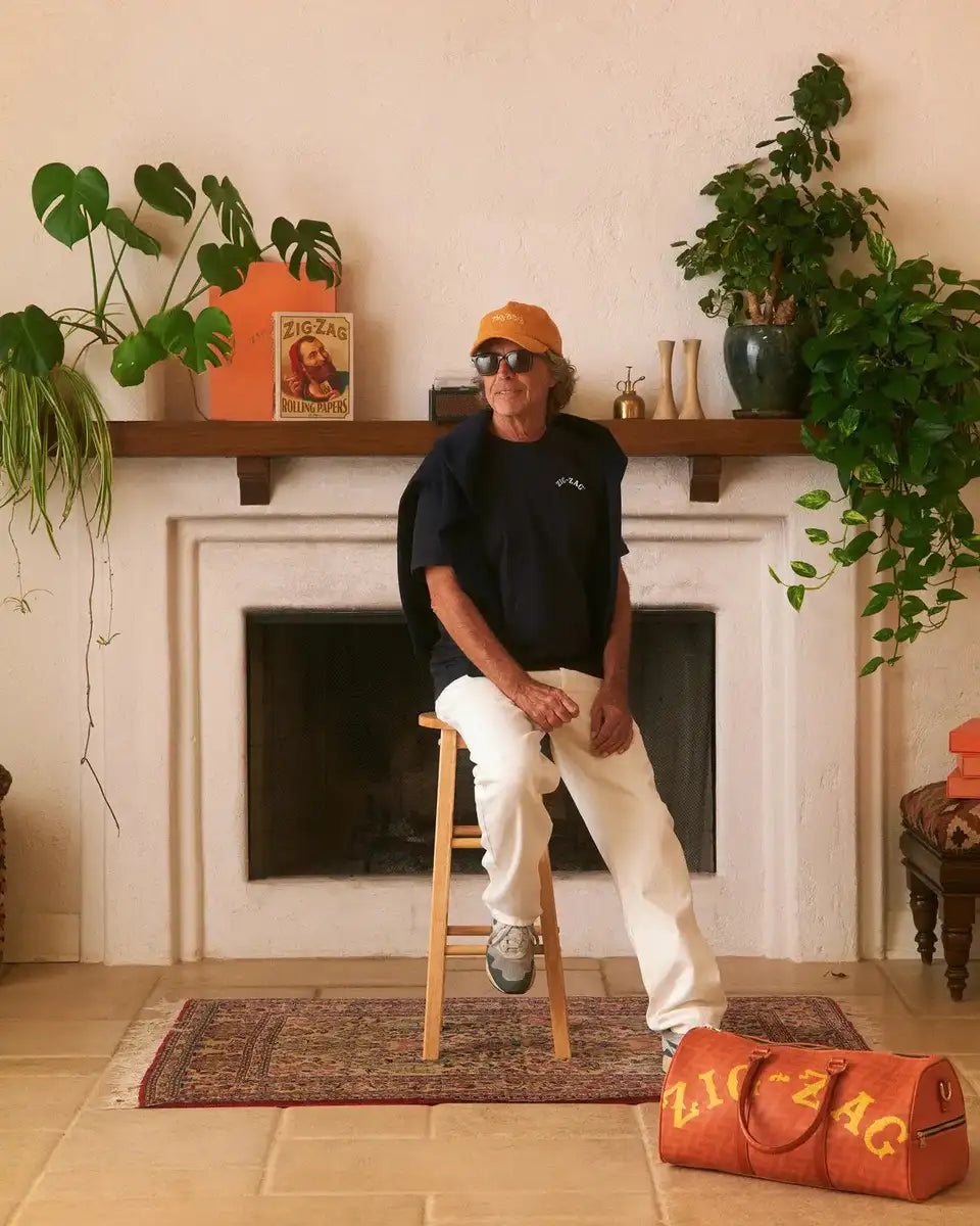 Zig-Zag orange cap worn by a seated individual in a stylish room with plants, branded decor, and a Zig-Zag duffel bag.