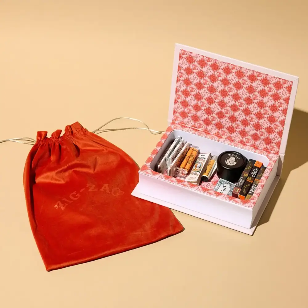 Zig Zag stash box set with vintage-style rolling papers and accessories, shown open next to a red velvet Zig Zag pouch.