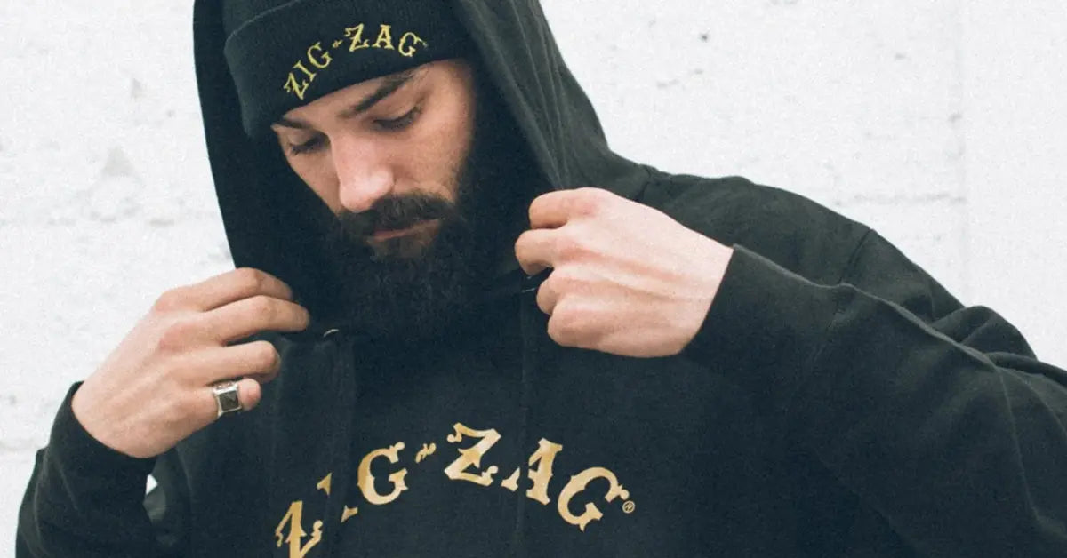 Man wearing a black Zig-Zag Logo hoodie and matching beanie adjusts his hood