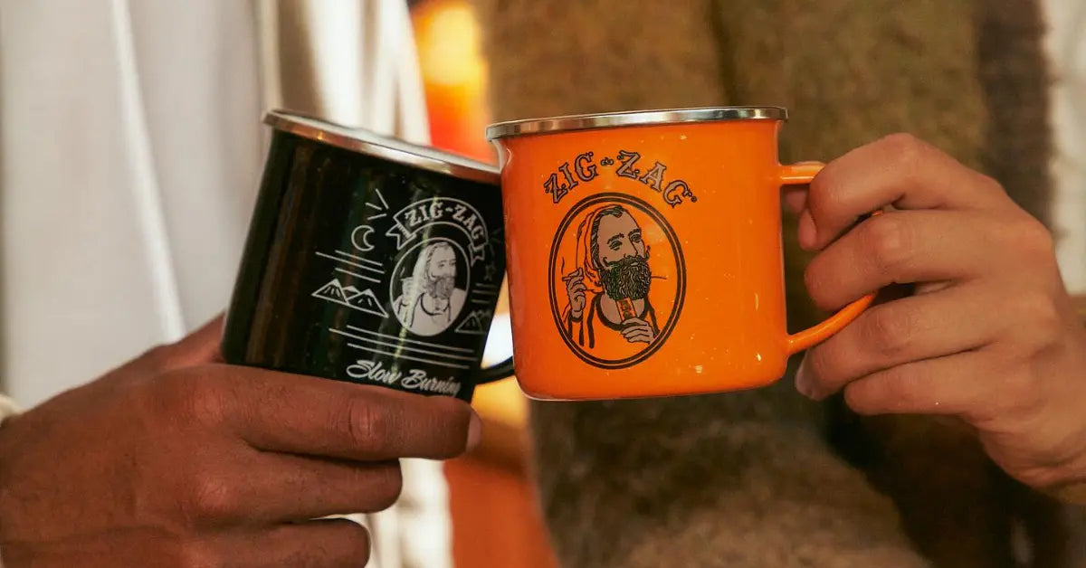 Two Zig-Zag logo mugs, one orange and one black, clinking together in a casual setting
