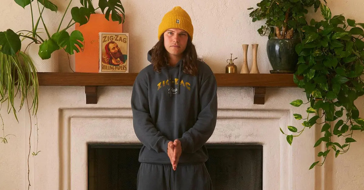 Zig-Zag branded hoodie and yellow beanie modeled in front of a fireplace with greenery