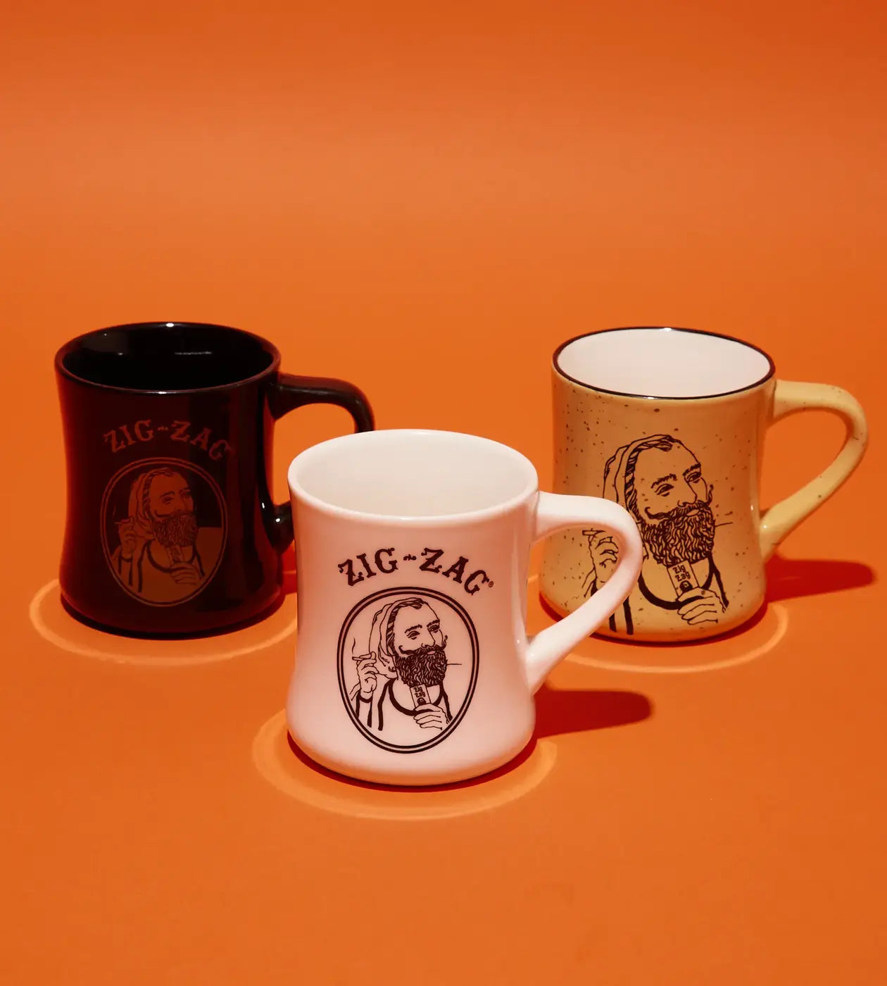 Zig-Zag mugs in black, white, and tan featuring bearded man illustrations on an orange background.