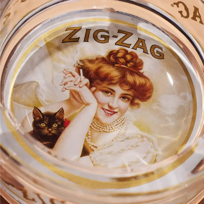 Close-up of a Zig-Zag ashtray featuring vintage artwork of a woman with red hair holding a cigarette and a black cat