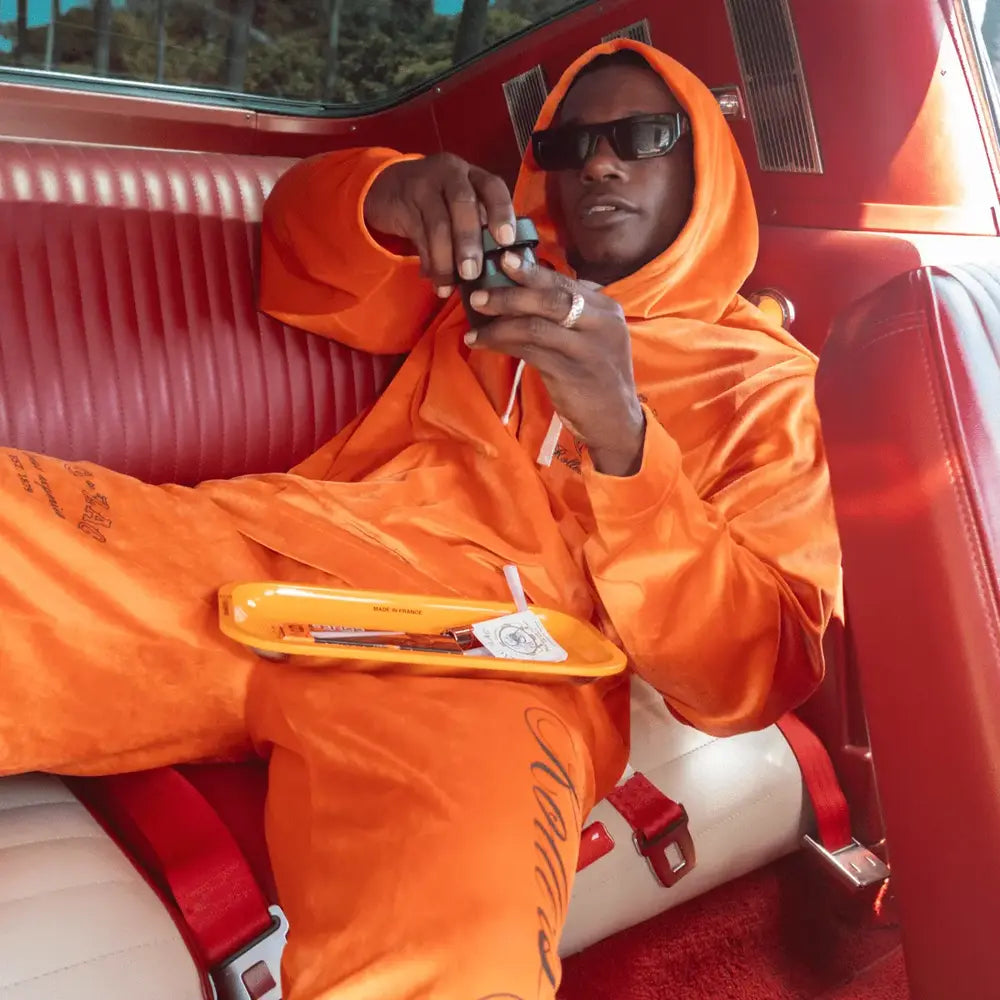 Man in an orange Zig-Zag hoodie and pants sitting in a retro car's red interior, holding an accessory